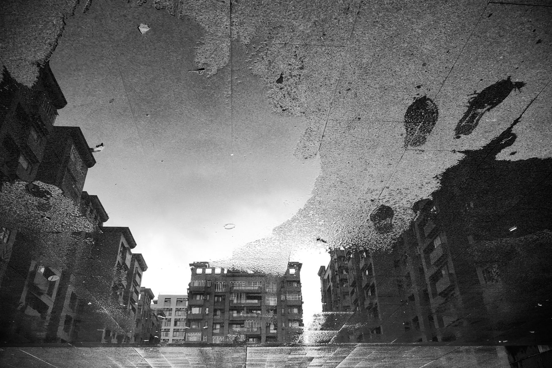 雨後水窪倒映的公寓街景，黑白